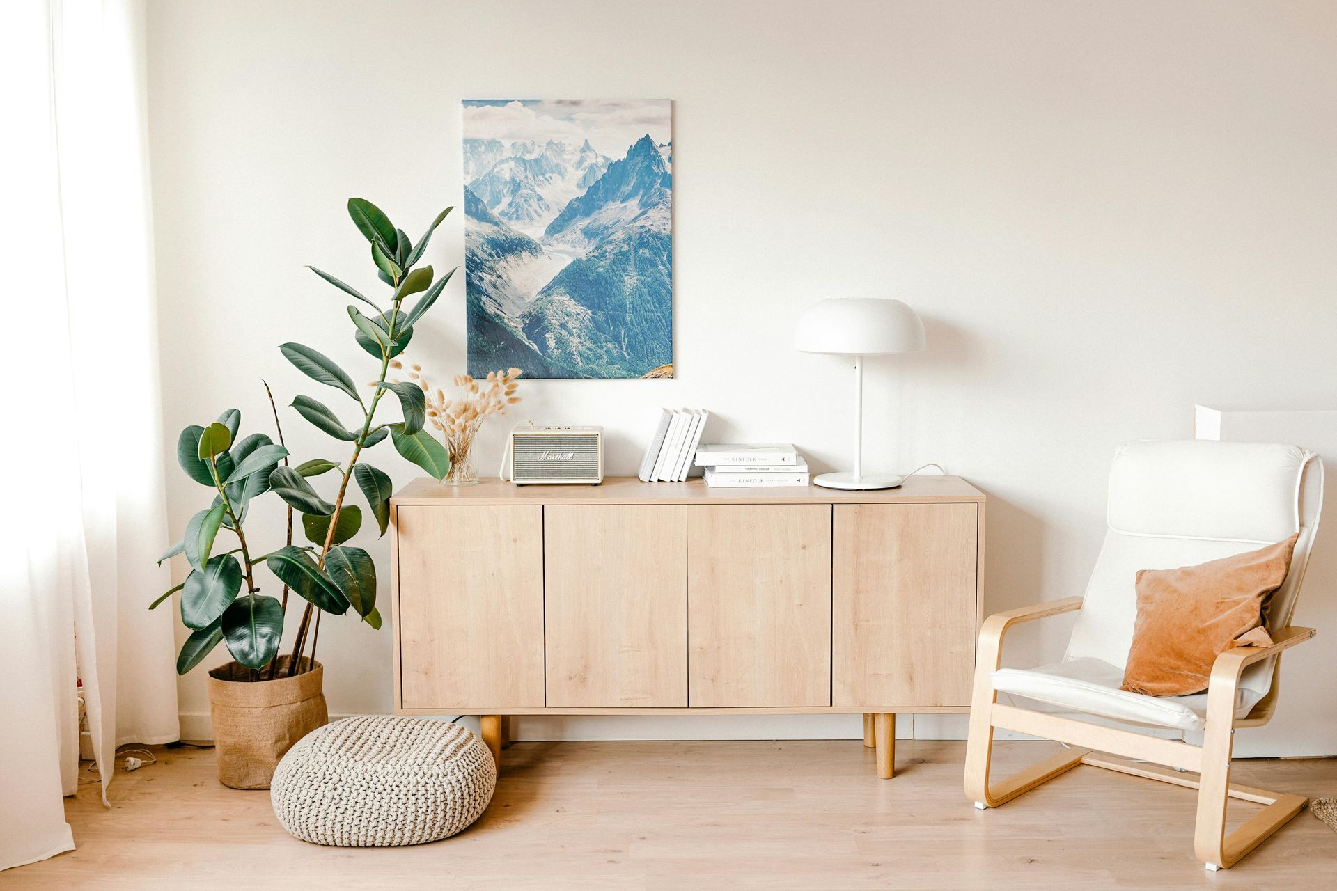 Bright living room with wooden cabinet, chair, potted plant, and wall art.