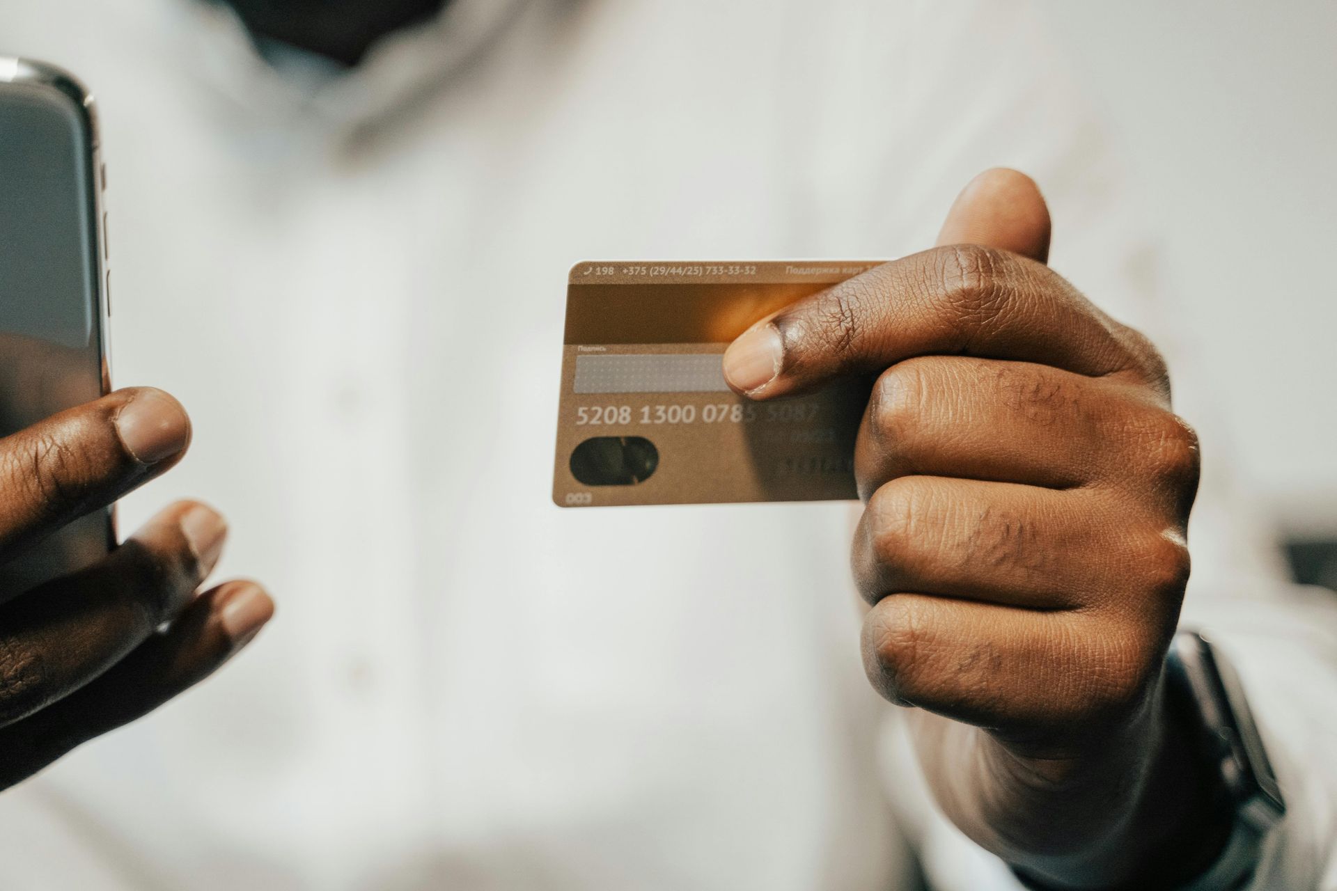 Person holding a gold credit card next to a smartphone.