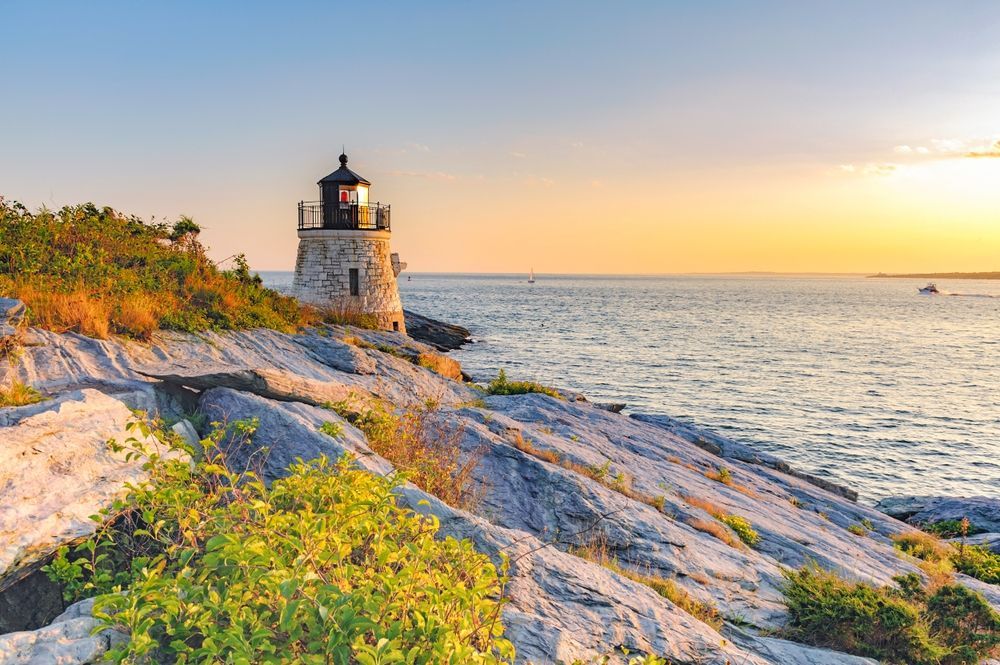 A lighthouse on a rocky cliff overlooking the ocean at sunset.