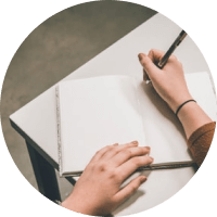 Hands writing in an open notebook on a white desk with a pen and ruler nearby