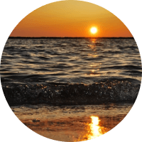 Sunset over the ocean, with orange sky and sun reflecting on gentle waves