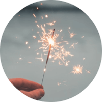 Hand holding a lit sparkler against a soft blue-gray background