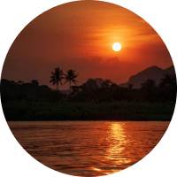 Orange sunset over a calm river with silhouetted palm trees and mountains