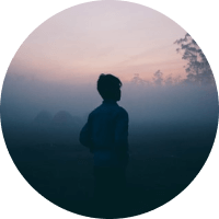 Silhouette of a person in a foggy field at dawn with a pink and blue sky