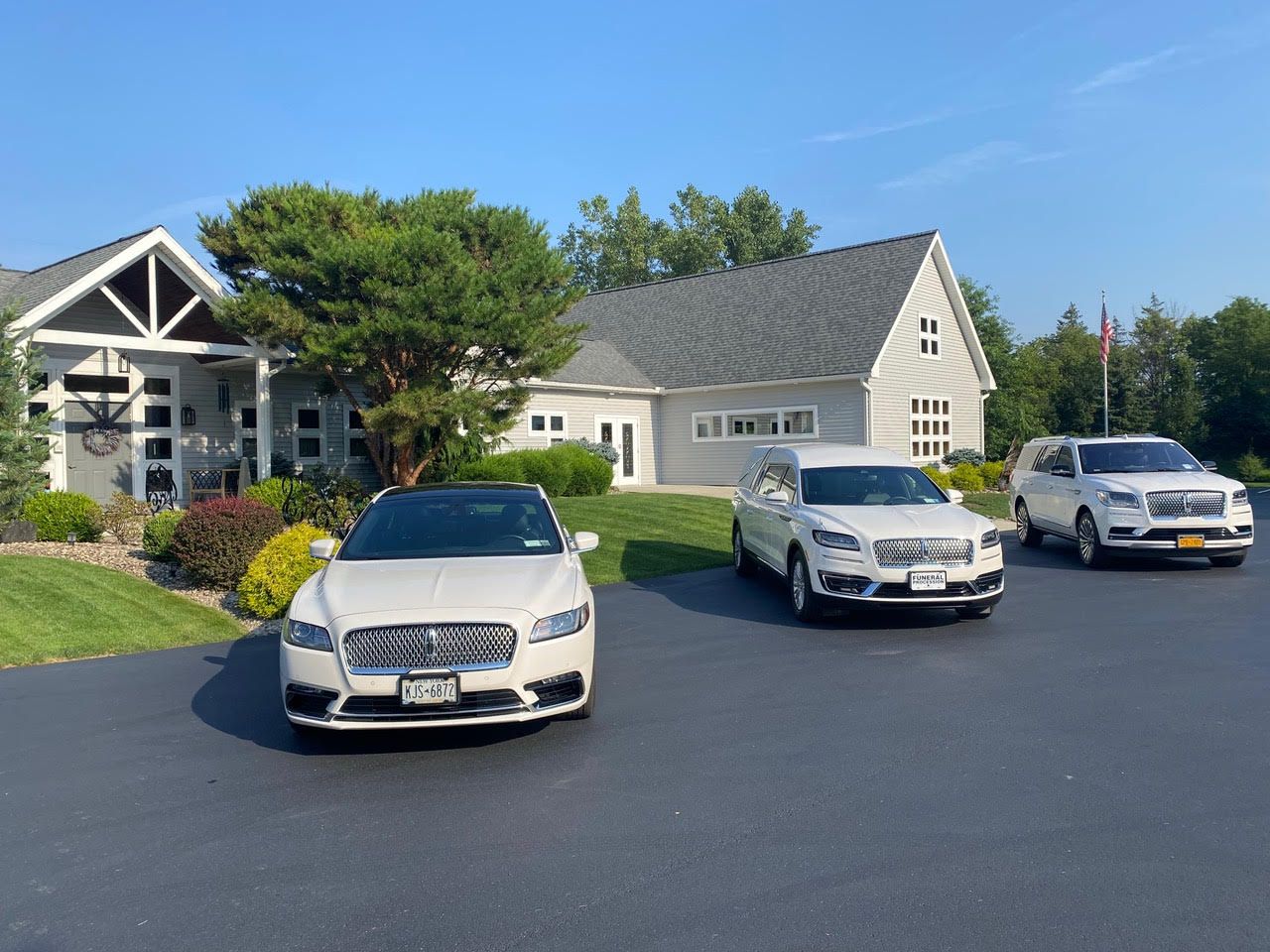 Three parked cars in front of a light-gray house with a driveway and landscaping