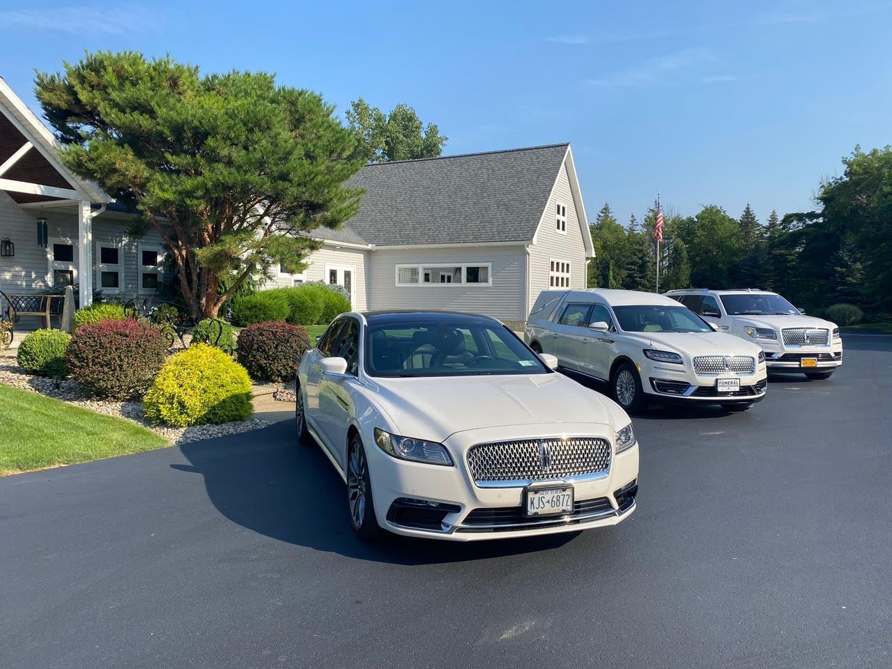Three cars parked in a driveway in front of a suburban house on a sunny day