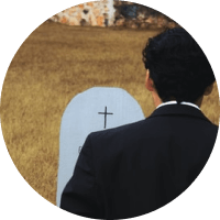 Person in a black suit facing a white cross on a tan wall