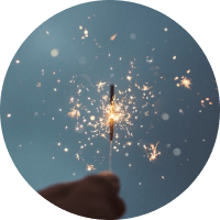 Hand holding a lit sparkler against a blue sky with glowing sparks