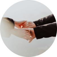 Two people holding hands in a close-up, with one in a dark sleeve and a soft neutral background