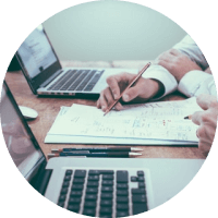 Hands writing on paperwork beside a laptop in a circular meeting-style photo