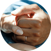 Two hands clasped together, one wearing a wedding ring
