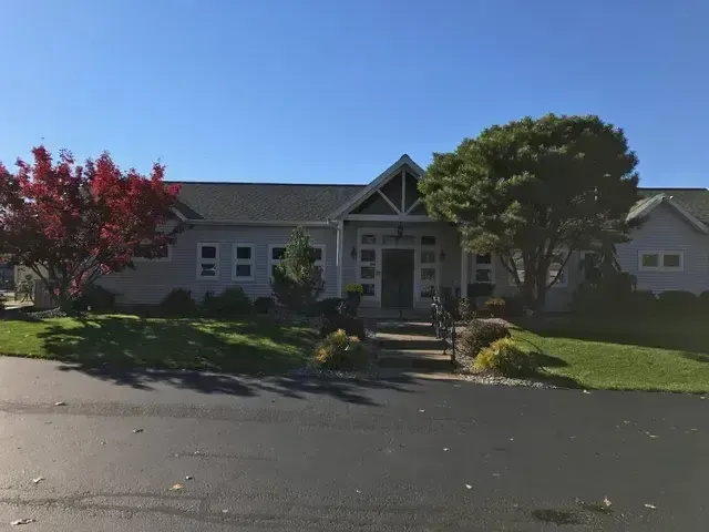 Single-story house with a front porch, trees, and a driveway under a clear blue sky