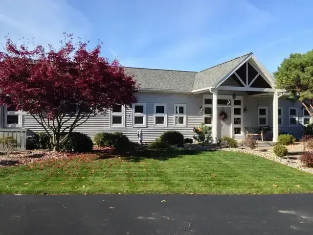 Suburban house with gray siding, white trim, red tree, and manicured lawn under a blue sky
