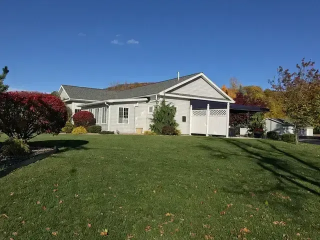 Single-story beige house with attached garage and green lawn under a clear blue sky