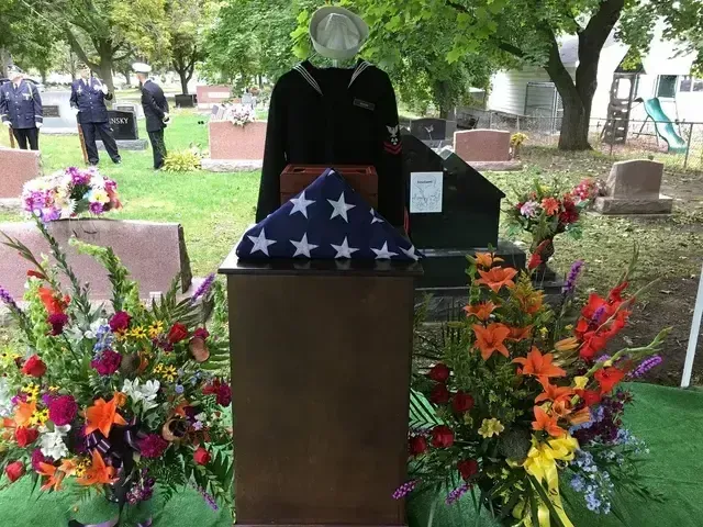 Memorial display with folded U.S. flag and floral wreaths at a cemetery grave site