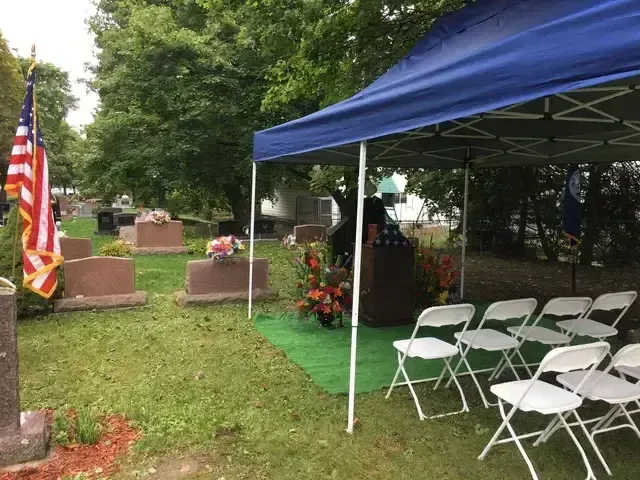 Memorial gravesites with an American flag and a blue canopy sheltering white folding chairs