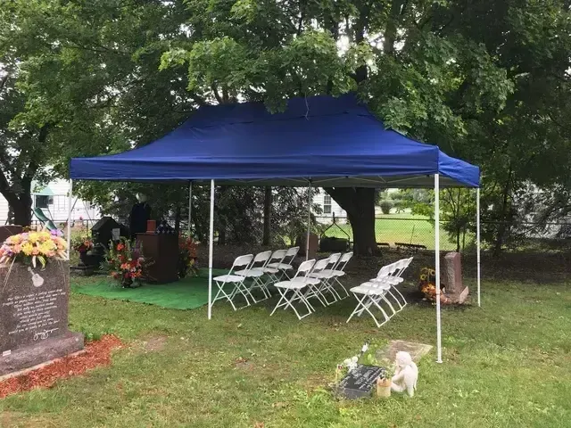 Blue canopy tent with white folding chairs set up on a grassy yard under a tree