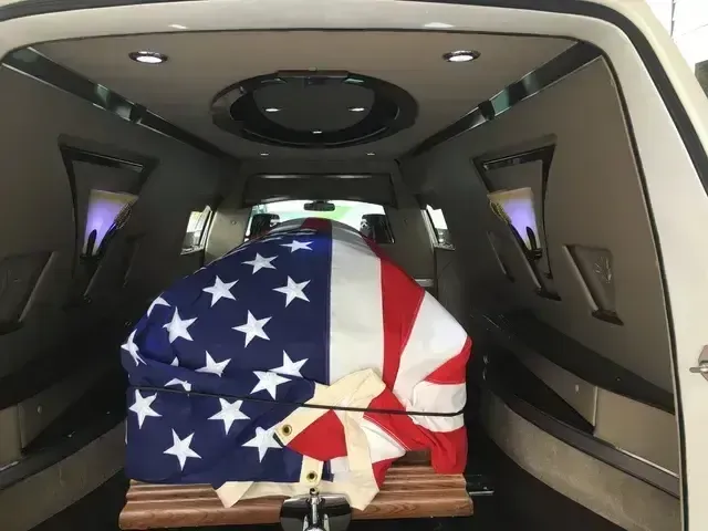 Flag-draped casket inside a hearse with wood-paneled interior