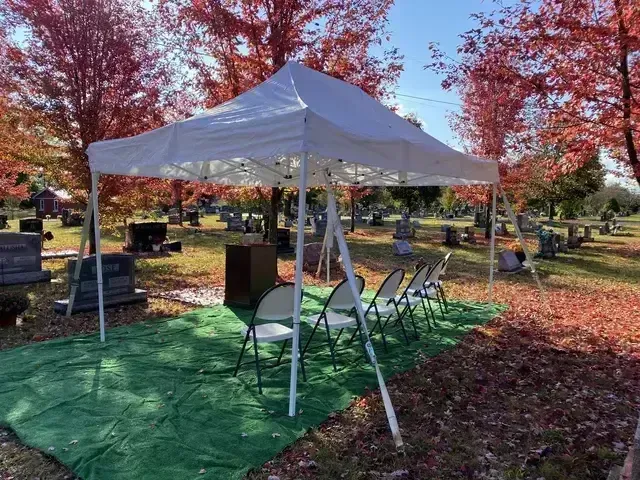 White event tent with folding chairs on green tarp in a leafy autumn park