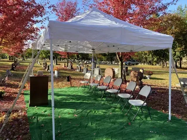 White canopy tent with folding chairs on green turf in a leafy outdoor autumn setting