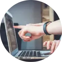 Hand pointing at a laptop screen, with another hand near the keyboard