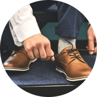 Person tying brown dress shoes while seated on a carpeted floor
