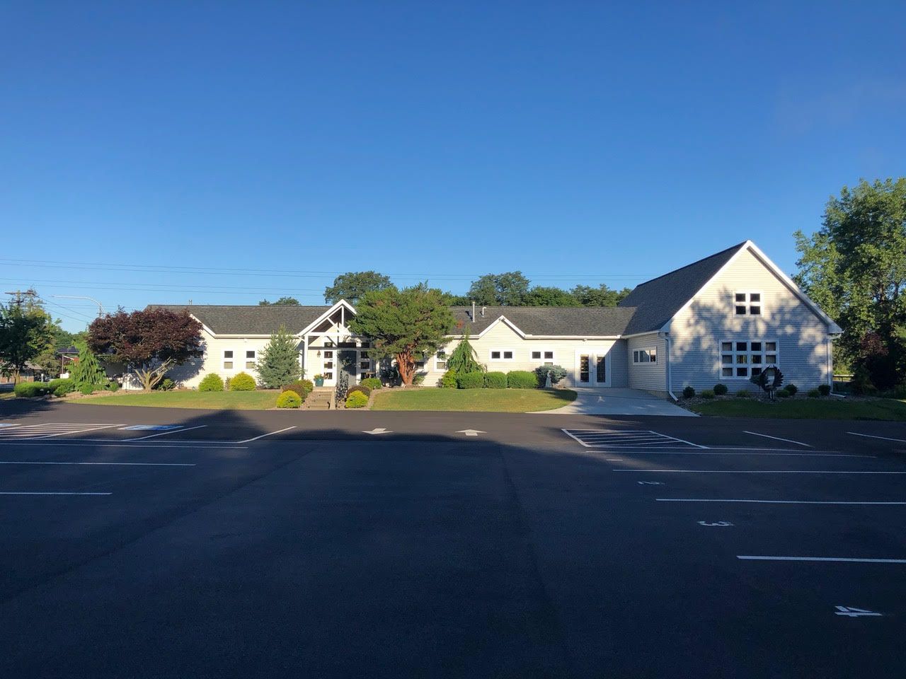 Large white buildings with gabled roofs beside an empty parking lot under a clear blue sky