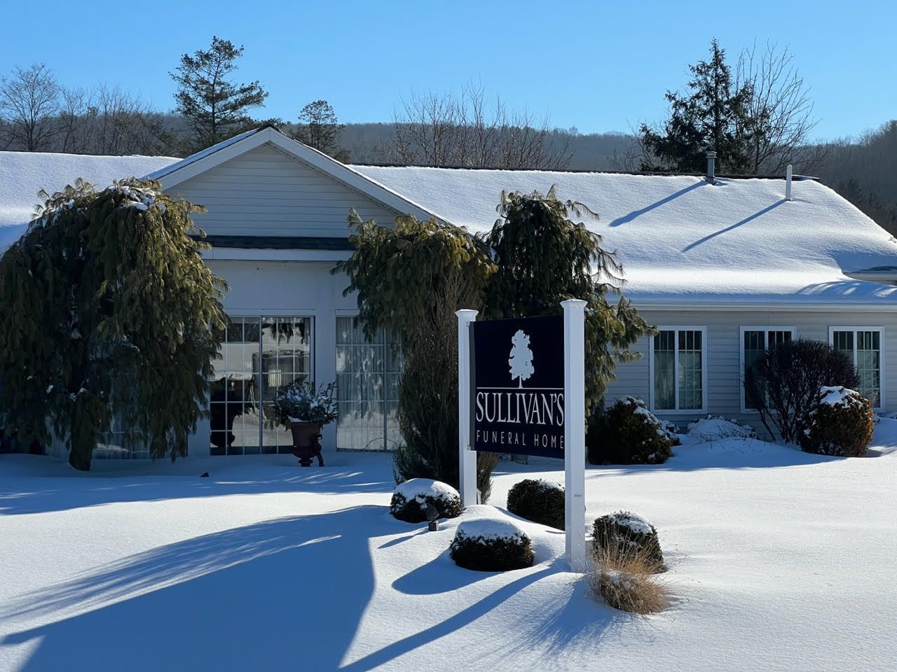Snow-covered building with a sign and landscaping in front on a sunny winter day