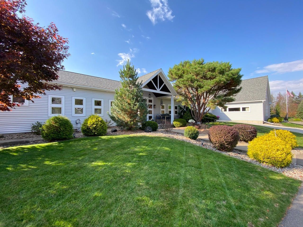 Suburban house with white siding, green lawn, and landscaped shrubs under a clear blue sky