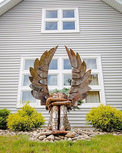 Rustic metal eagle sculpture with spread wings in front of a gray house with white windows