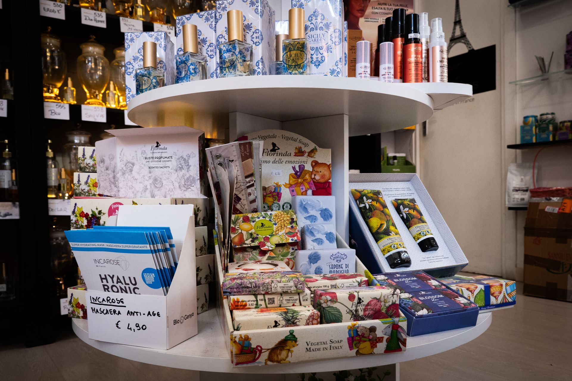 Uno scaffale circolare in un negozio, pieno di vari articoli da regalo come saponi, profumi e scatole.