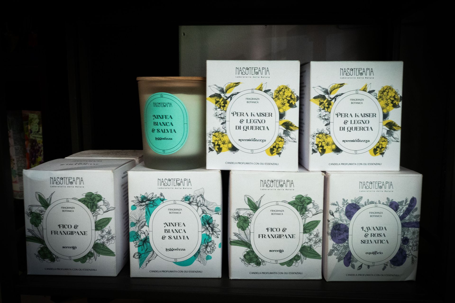 Candele e scatole su uno scaffale. Scatole bianche con illustrazioni floreali. Una candela in un barattolo di vetro.