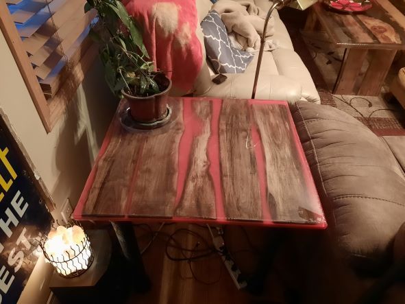 Wood and pink resin table with a potted plant on a tan couch.