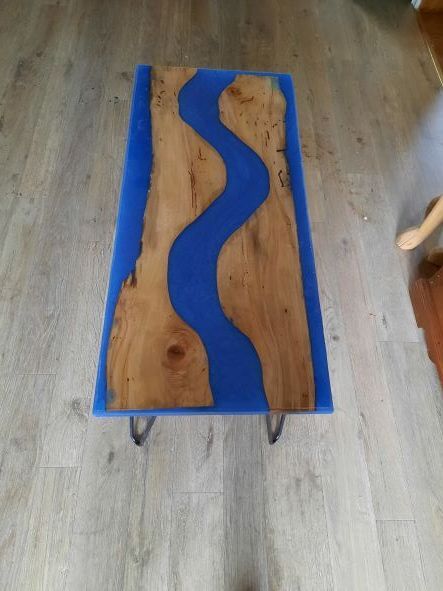 A rectangular wooden table with a blue resin river running through it, sitting on metal legs.