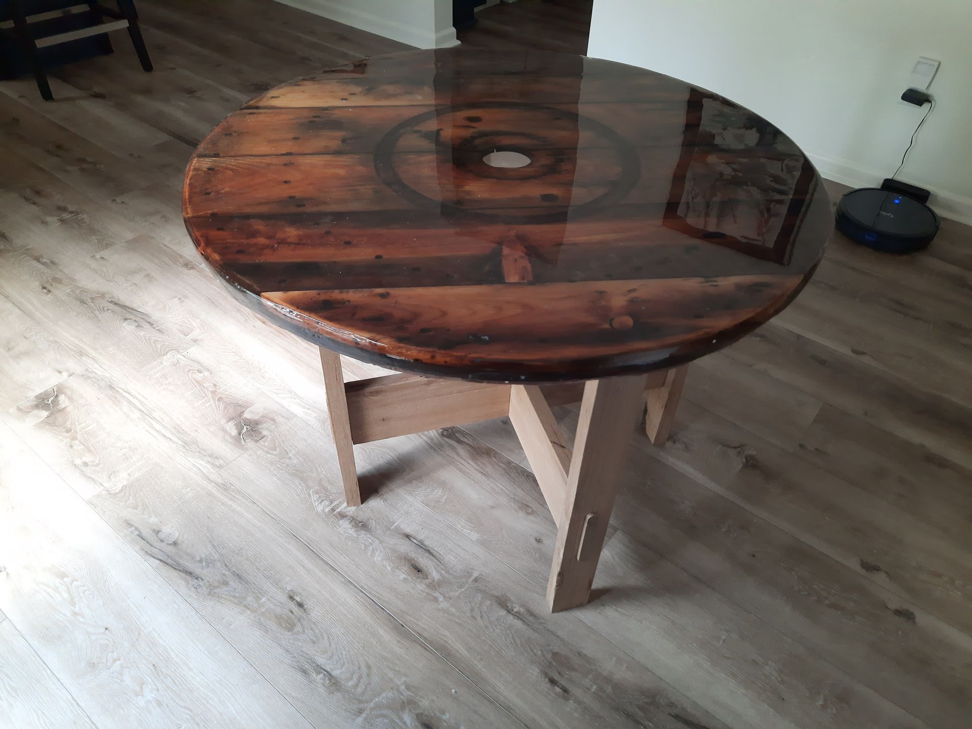 Round wooden table with a glossy, dark wood top and light wood legs on a wood floor.