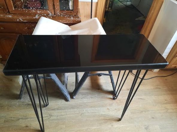 Black rectangular table with hairpin legs in front of a chair, indoor setting.