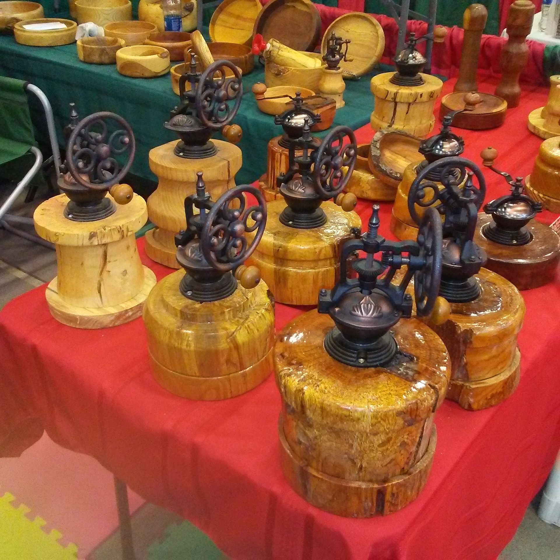 Coffee grinders mounted on wooden bases displayed on a red tablecloth.