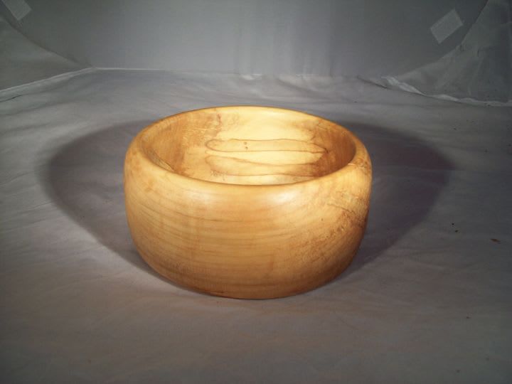 Wooden bowl, light brown color, circular shape, sits on a white surface.