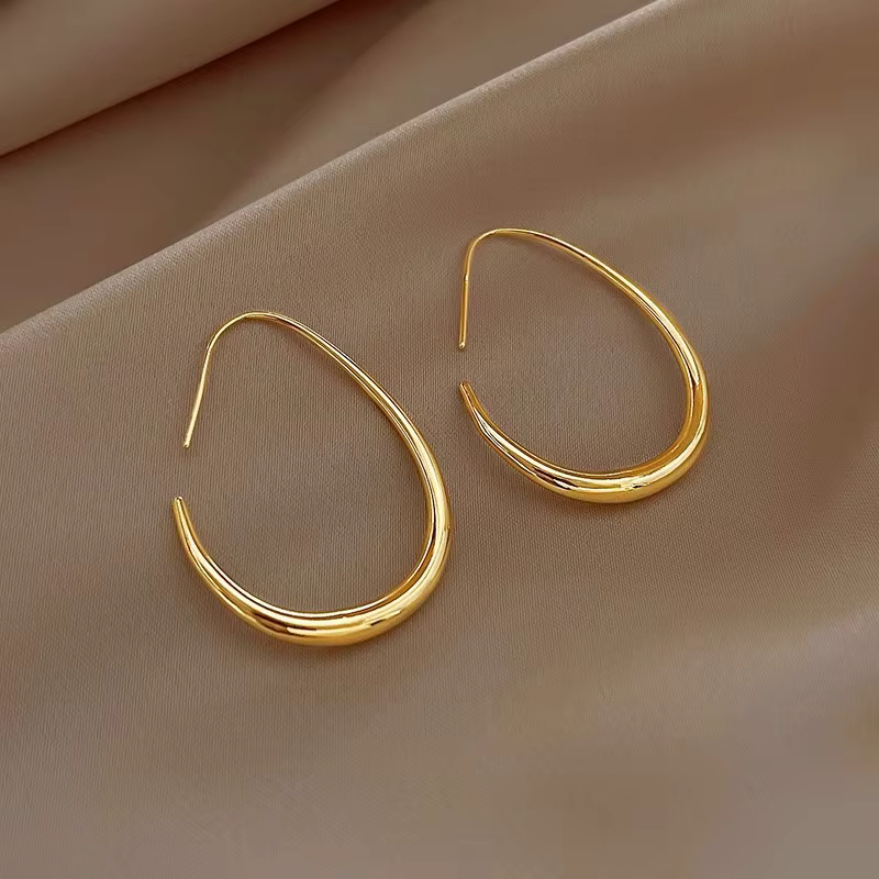 Pair of gold teardrop hoop earrings on beige fabric background