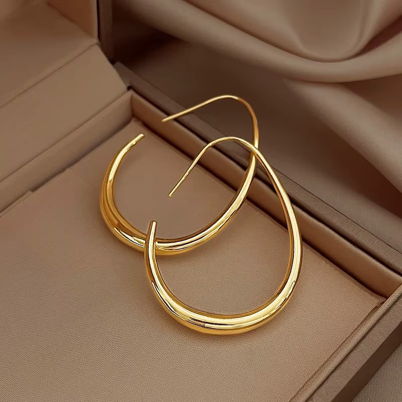 Two gold hoop earrings in a tan jewelry box with soft draped fabric backdrop