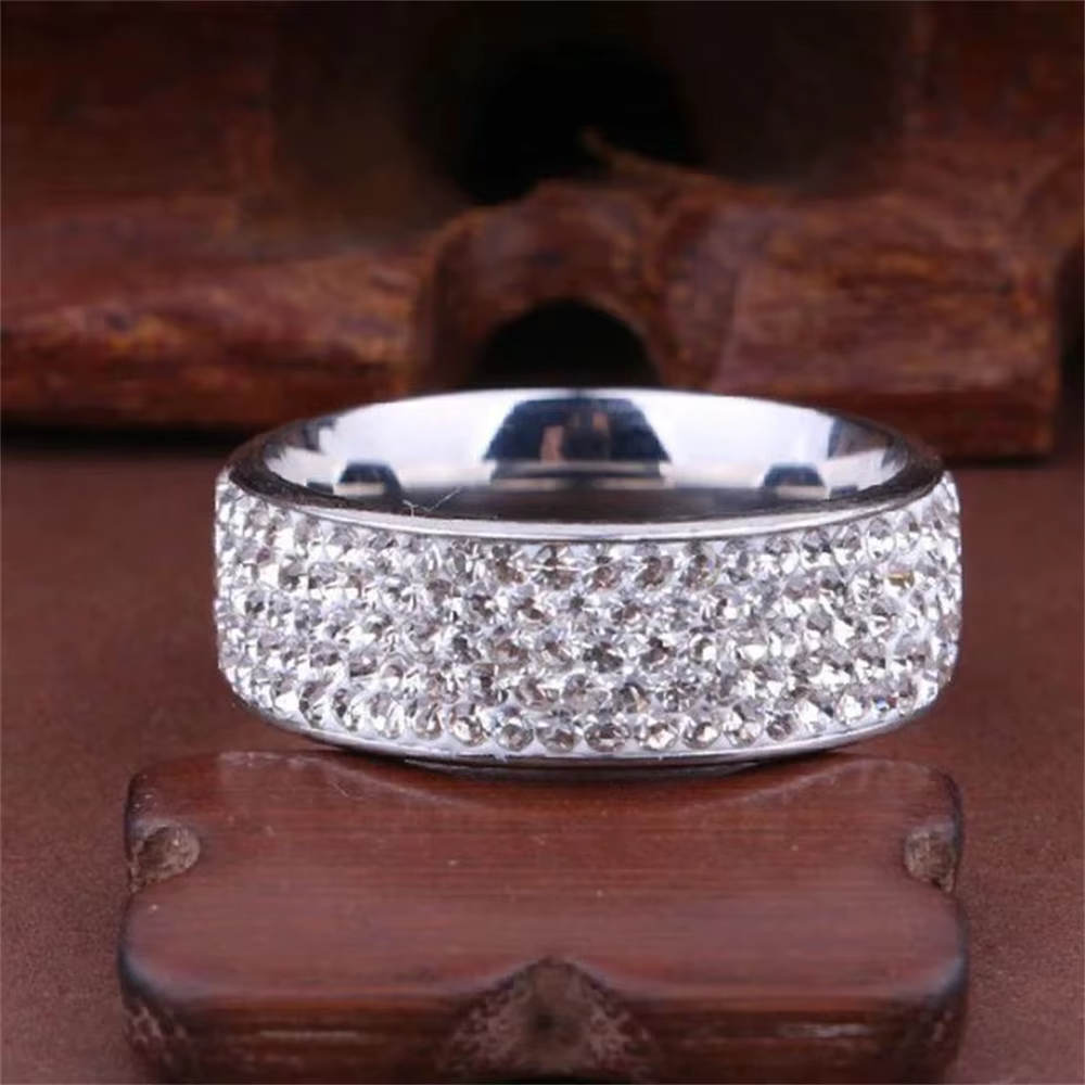 Pair of silver and gold wide band rings covered in sparkling stones on a dark red background