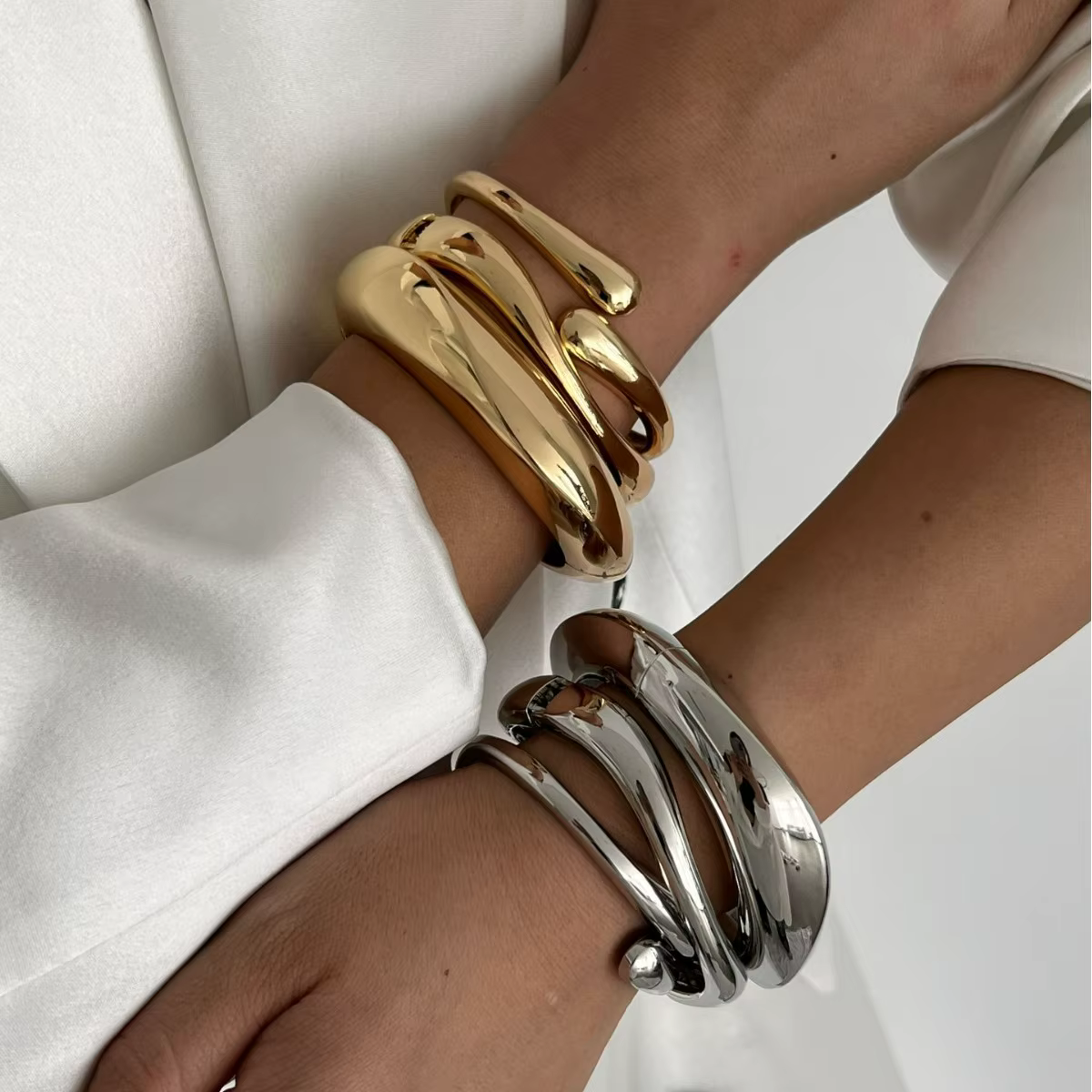 Close-up of stacked gold and silver bangles on crossed wrists against a white background