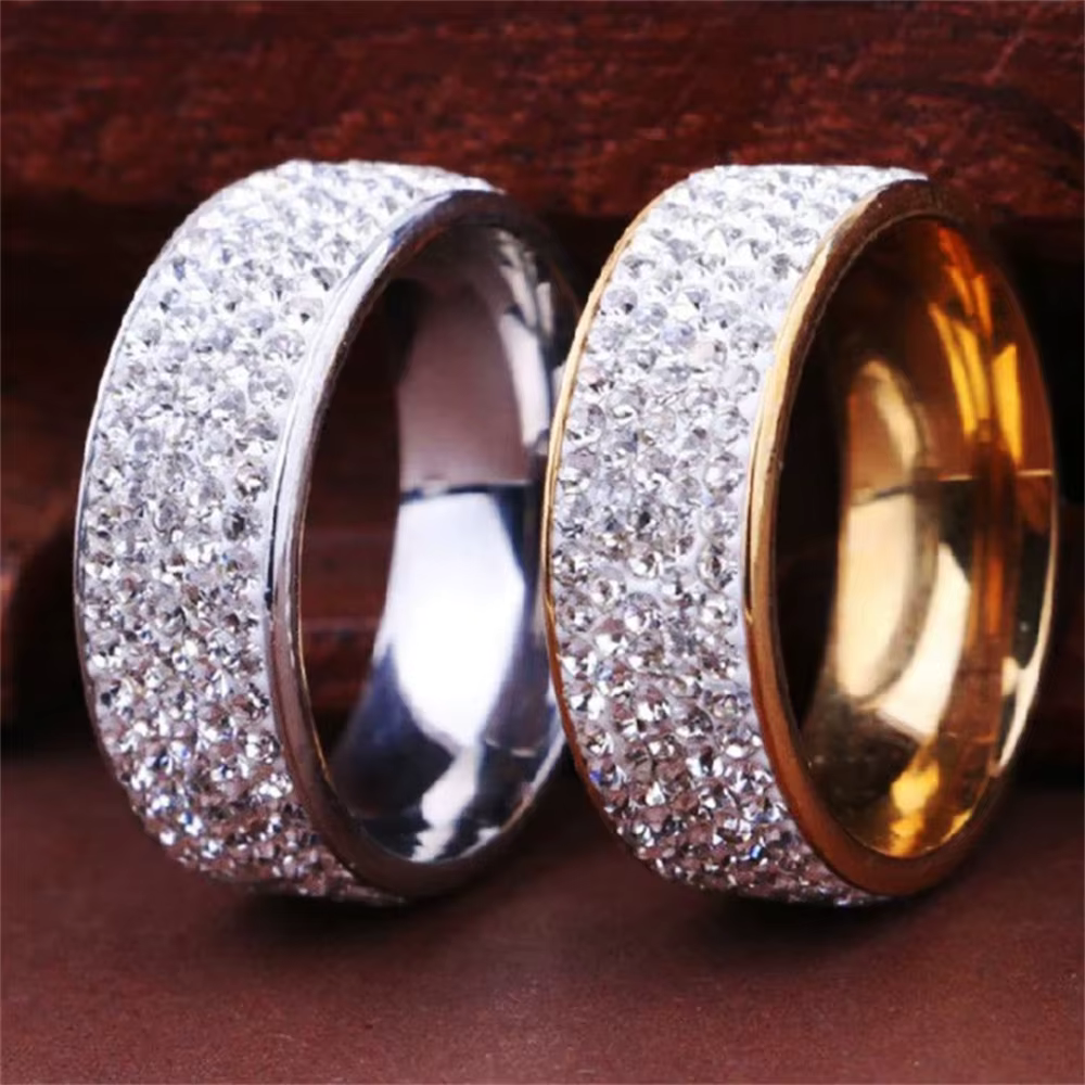 Pair of silver and gold wide band rings covered in sparkling stones on a dark red background