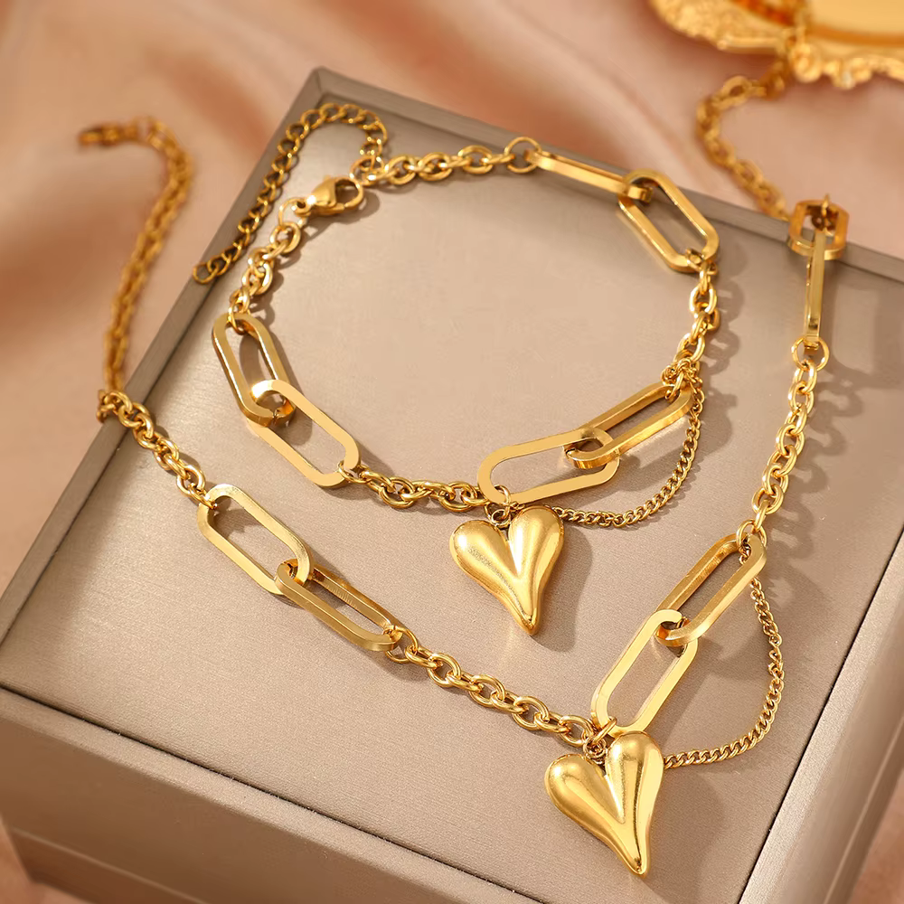 Gold heart pendant necklace and matching bracelet on a beige jewelry box.