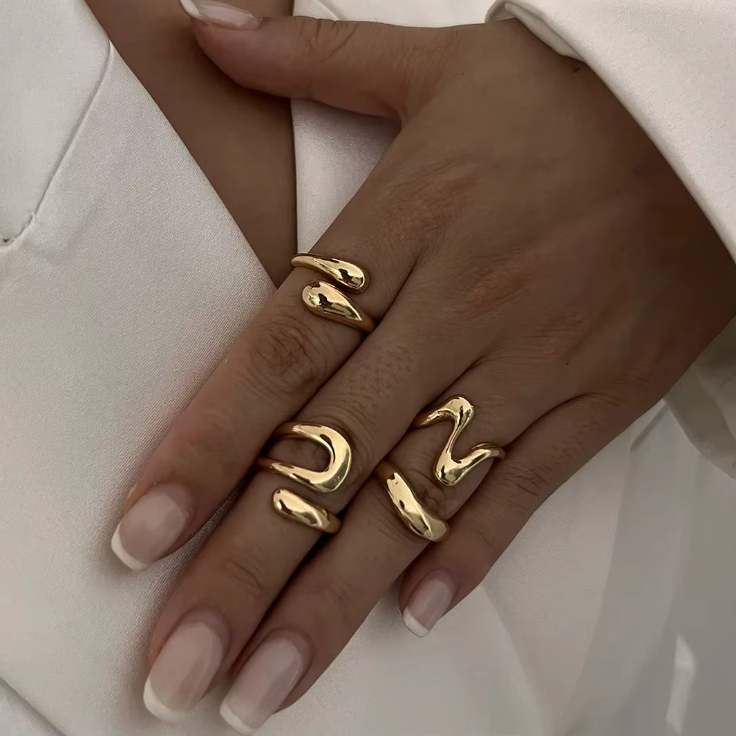 Two hands with gold abstract rings resting on a white textured fabric background