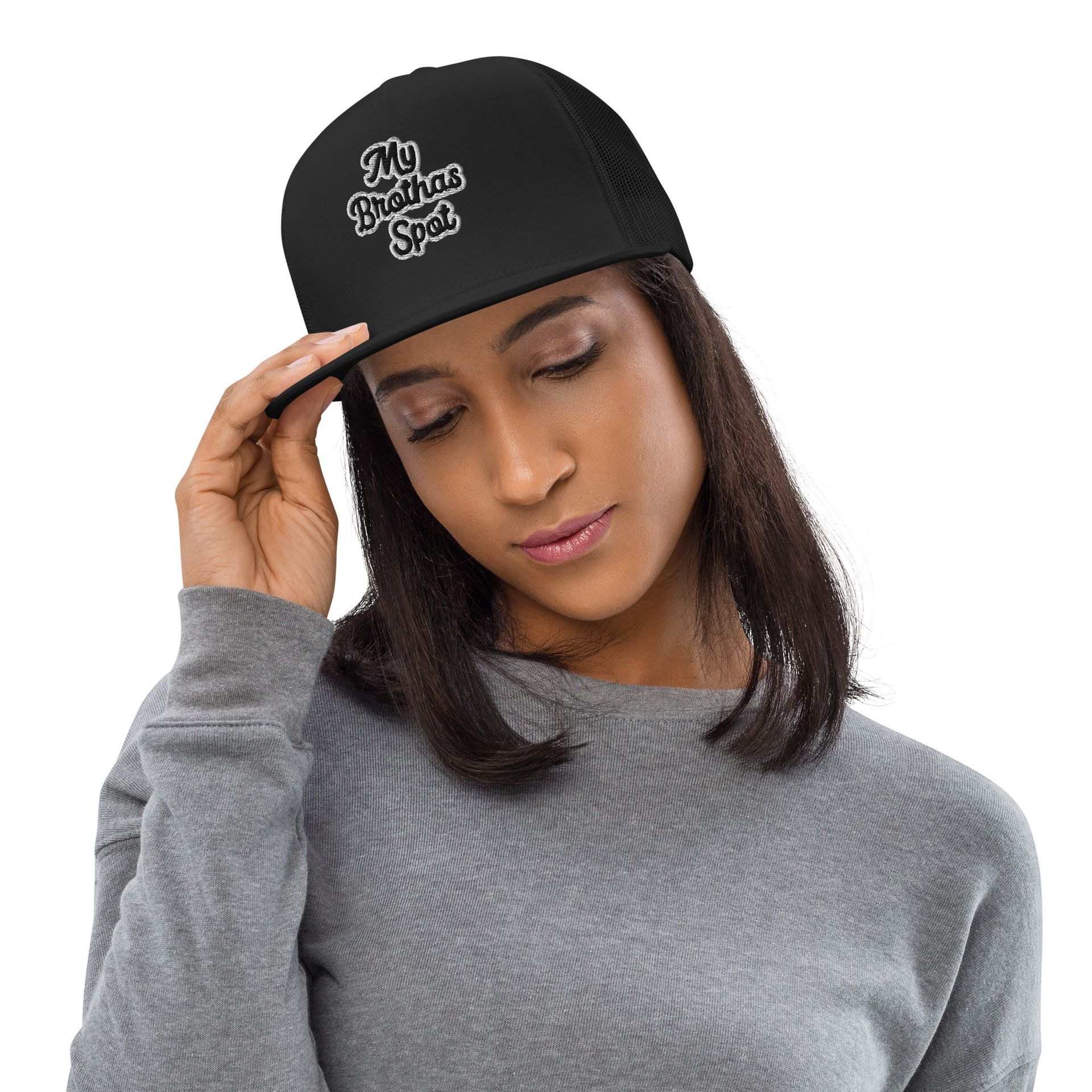 Woman in a gray sweater adjusting a black cap, looking downward on a white background