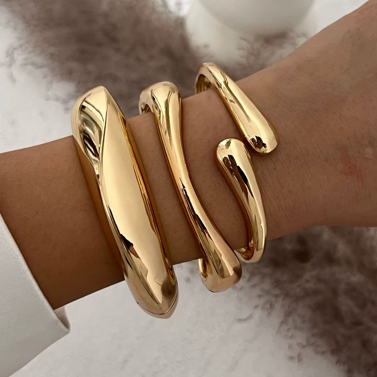 Gold abstract snake-shaped bracelet on a wrist against a soft neutral background