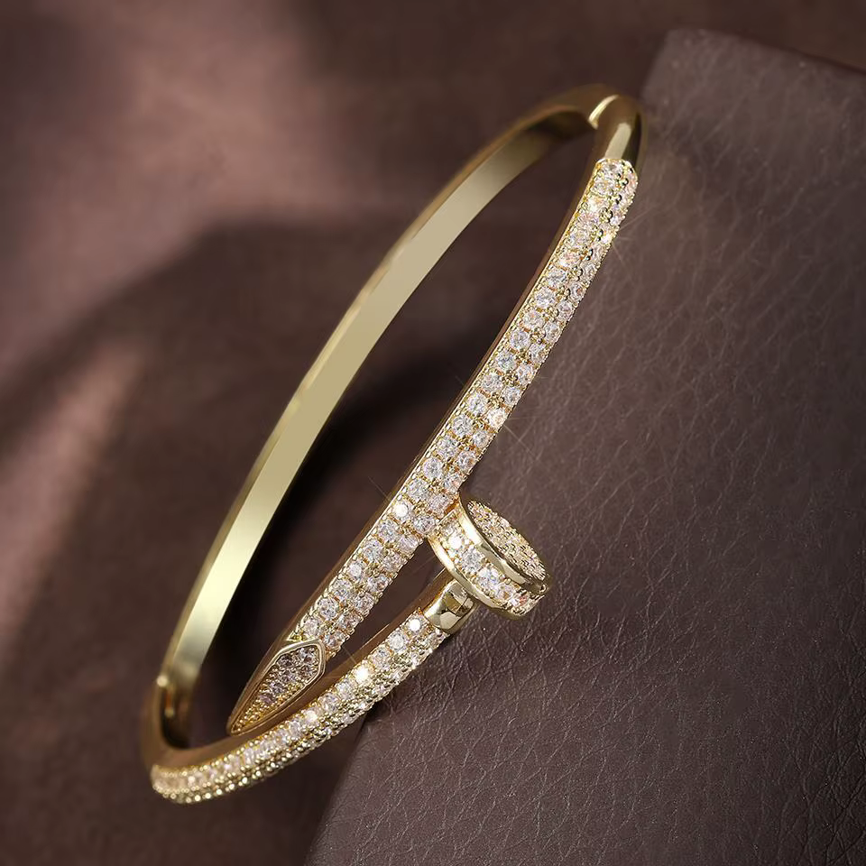 Gold bangle bracelet with pavé crystals and a central oval detail on a soft brown background