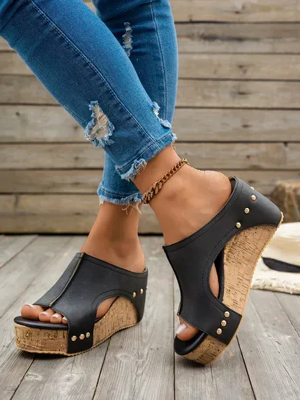 Black wedge sandals with cork soles worn with ripped jeans on a wooden floor