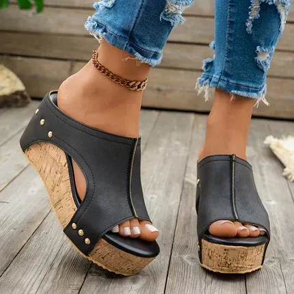 Black wedge sandals with cork soles worn with ripped jeans on a wooden floor